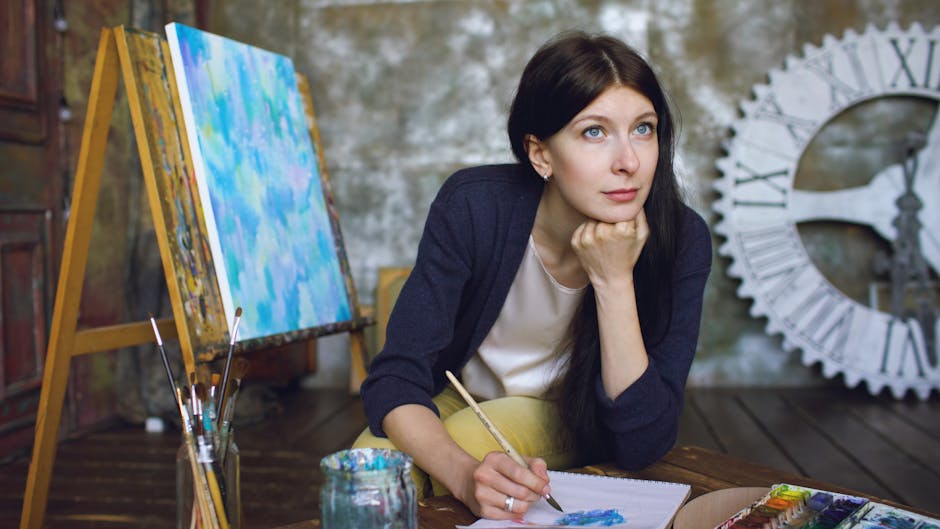 A thoughtful female artist in her studio surrounded by painting supplies, deeply engrossed in her art.