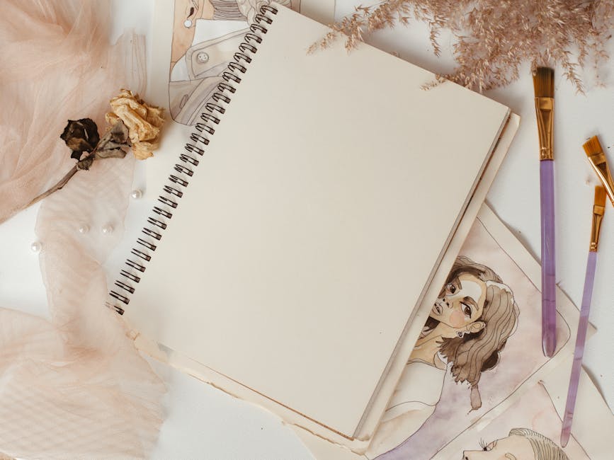 Elegant composition of art supplies including a sketchbook, paintbrushes, and dried flowers on a white surface.